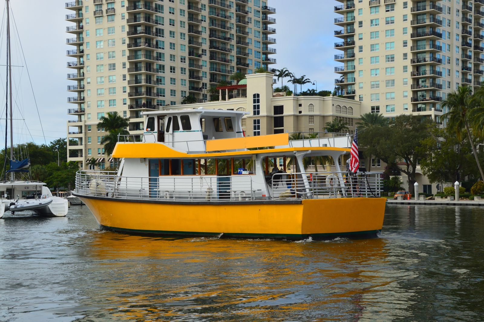 A yellow and white water taxi cruising past riverside apartment towers and a moored catamaran